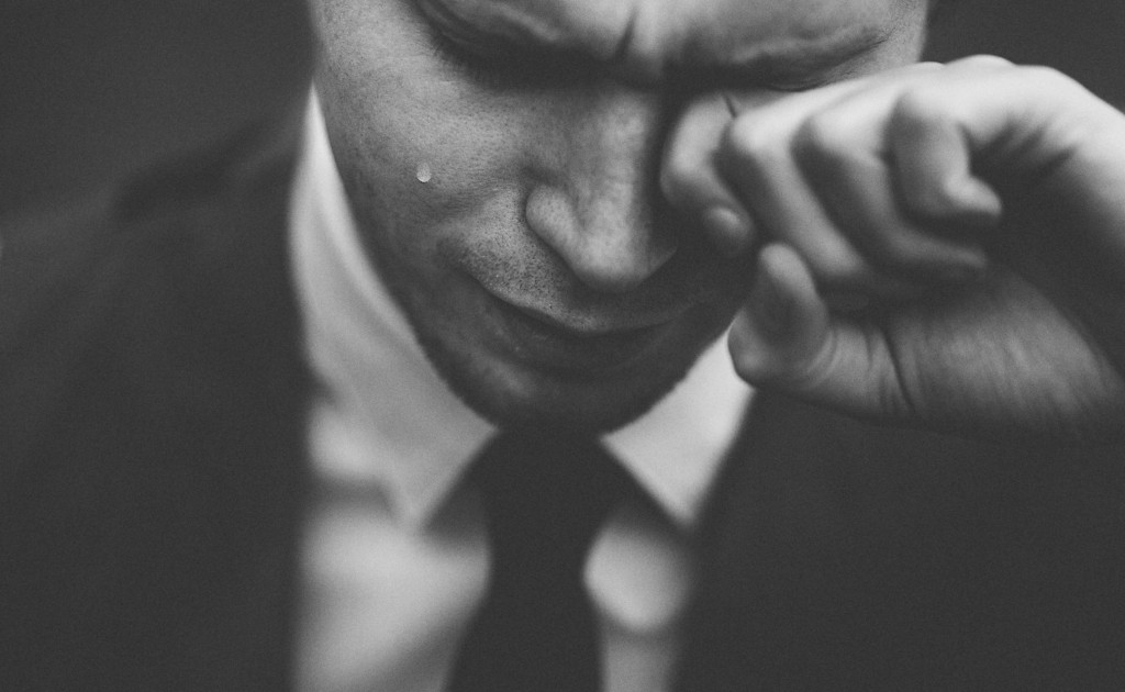 photograph of a man in a suit and tie, crying. Photo by Tom Pumford, from Unsplash.